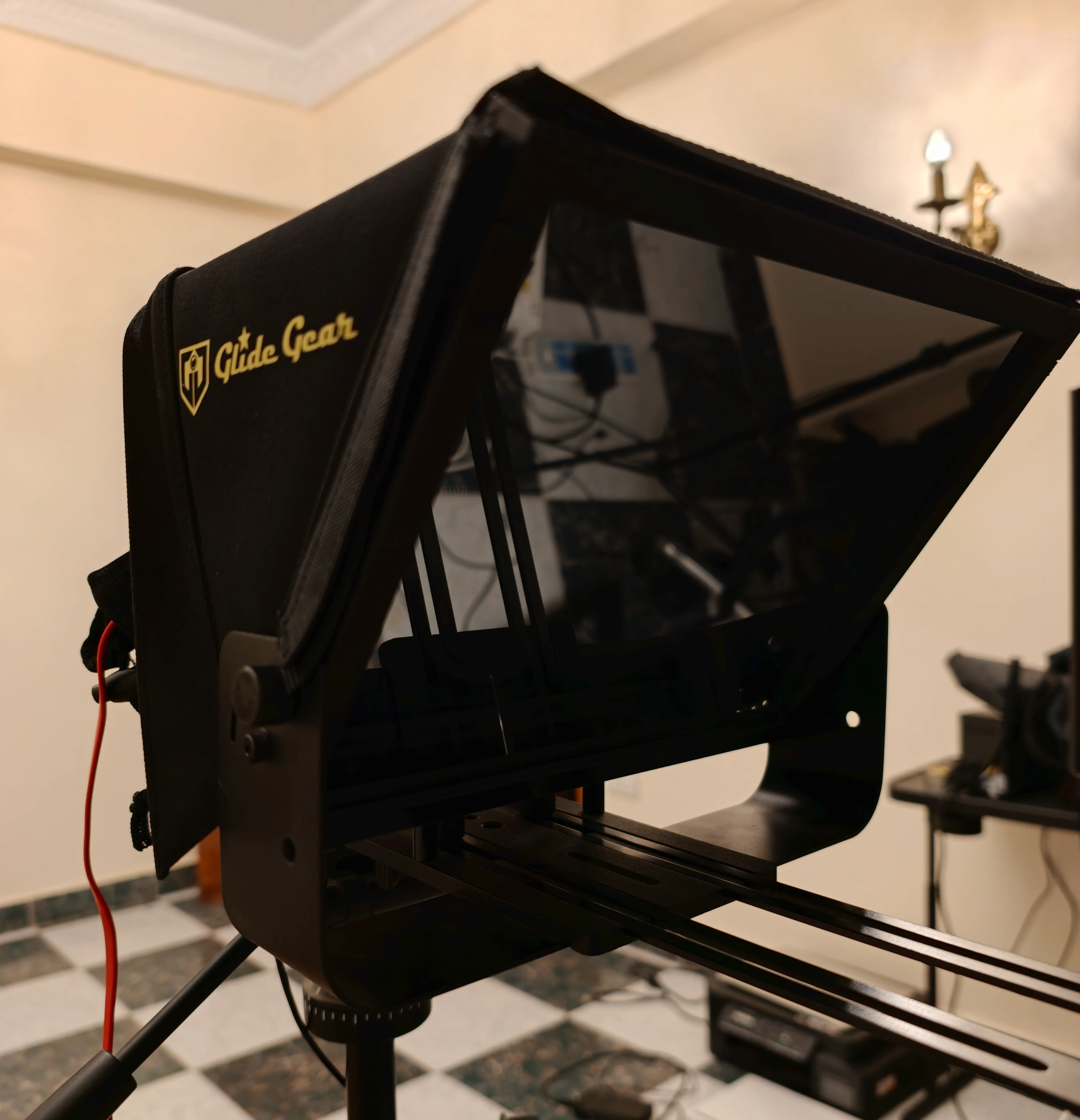 The teleprompter rig: a beam-splitter hood on a tripod, glass angled over a tablet tray.